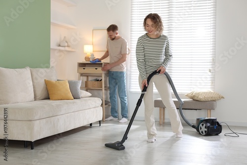 Woman vacuuming and man wiping dust at home, selective focus