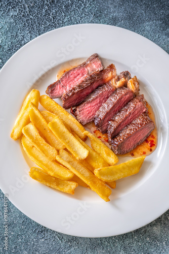 Sliced grilled beef steak with fries and chili sauce gourmet meal top view