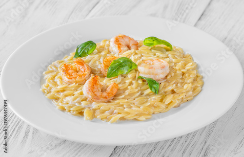 Creamy orzotto pasta topped with grilled prawns and fresh basil on rustic wooden table