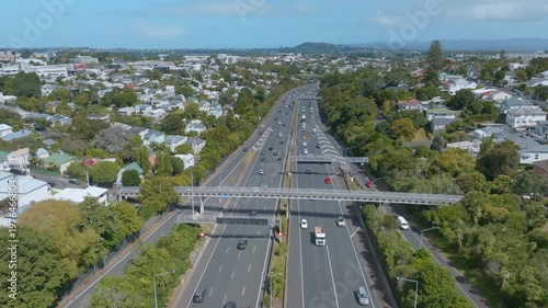 Cars travel on the busy Northwestern highway in Auckland, New Zealand, connecting the city to residential areas. The scene shows the flow of traffic and urban landscape.