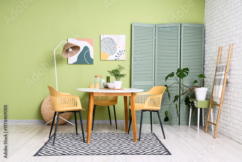 Interior of stylish dining room with table, lamp and green folding screen