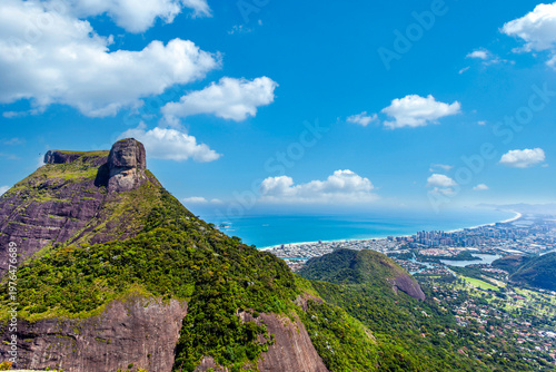Breathtaking aerial view of Pedra da Gávea mountain overlooking Barra da Tijuca beach and the Atlantic Ocean in Rio de Janeiro, Brazil. A stunning landscape featuring lush green peaks and city.