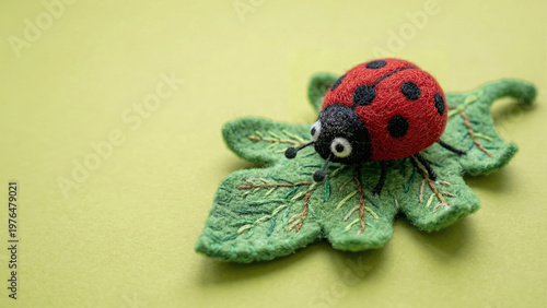 Needle felted wool sculpture of a red ladybug resting on an embroidered green leaf against a light green background. Handmade textile art featuring a soft plush insect craft.