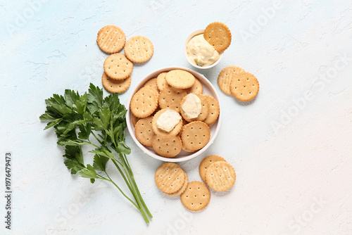 Tasty crackers with bowl of sauce and parsley on light blue background