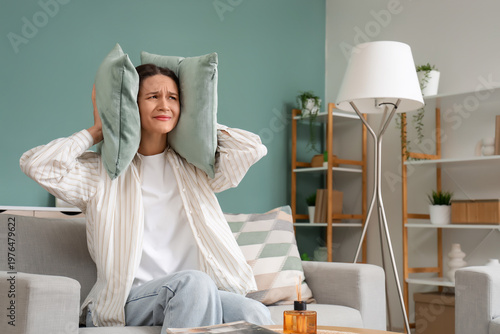 Photos Young woman covering her ears with pillows because of noisy neighbours on sofa a
