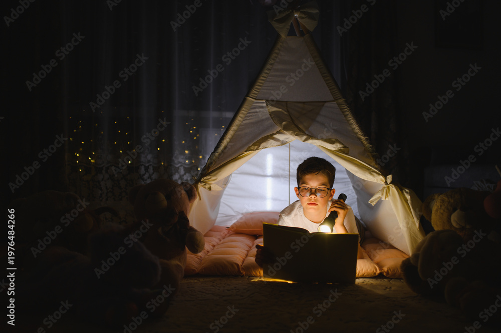 Obraz premium Boy reading book inside teepee tent at night