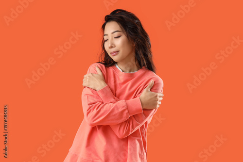 Bild auf Leinwand Young Asian woman hugging himself on orange background