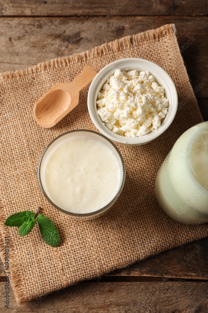 Naklejka premium Glass of fresh kefir with mint and bowl of cottage cheese on wooden background