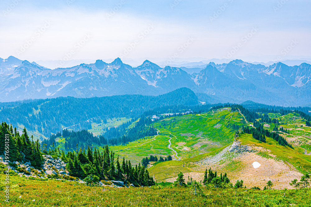 Fototapeta premium Rolling green slopes with a winding path and extensive mountain ranges stretching across the horizon.