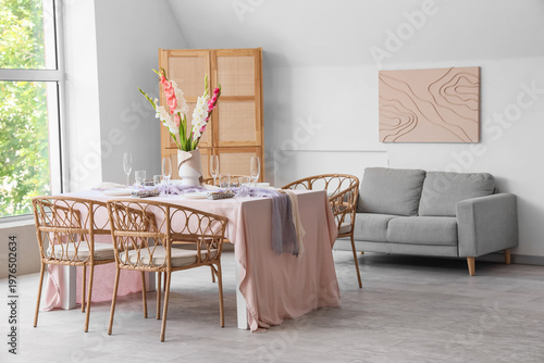 Served dining table with plates and beautiful gladiolus flowers in interior of stylish living room