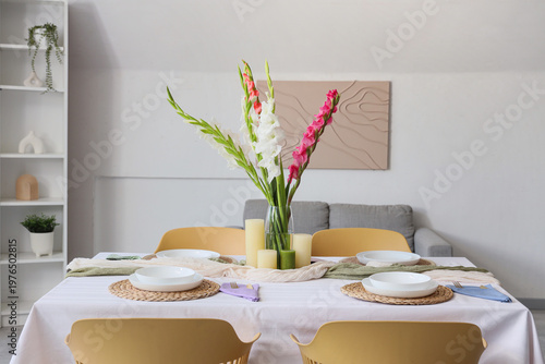 Elegant table setting with plates, candles and beautiful gladiolus flowers
