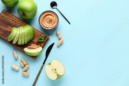 Wooden board with fresh apple slices and bowl of sweet peanut butter on blue background