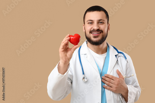 Young happy male doctor with stethoscope and red heart on beige background. W...