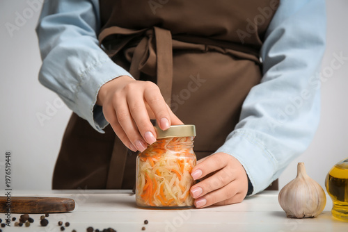 Woman cover with lid jar of sauerkraut on table in kitchen. Closeup