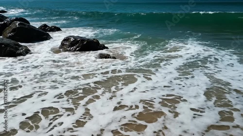 Ocean waves crashing over rocks on a sandy tropical beach shoreline