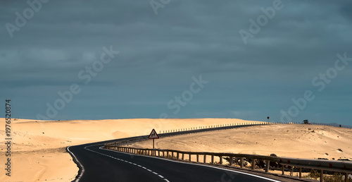 An asphalt road among desert with sandy dunes.