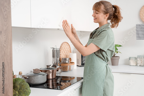 Young woman wiping cupboard...