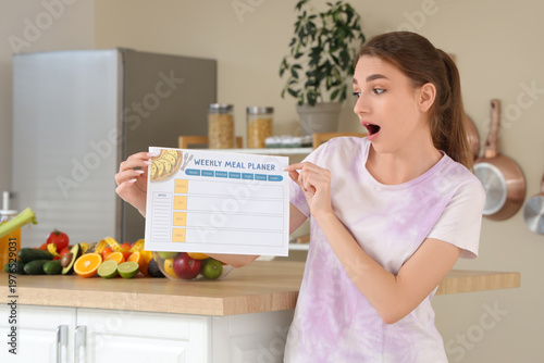 Shocked young woman with weekly meal planer in kitchen. Diet concept