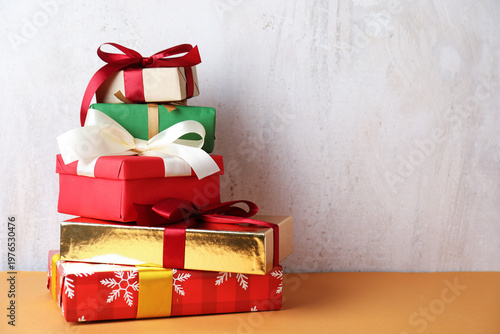 Stack of many gift boxes on orange table near grey wall, space for text. Merry Christmas and Happy New Year