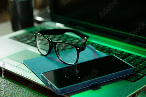 Business closeup portrait in different light with same camera manual and composition. Glasses, mobile phone placed on laptop keyboard. Research, study, work concept in green lighting