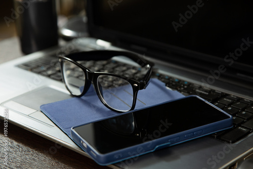 Business closeup portrait in different light with same camera manual and composition. Glasses, mobile phone placed on laptop keyboard. Research, study, work concept in natural lighting