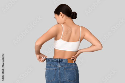 Fotografia Young woman in loose jeans after weight loss on light background, back view