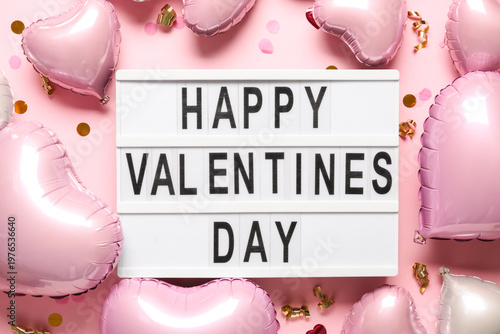 Board with text HAPPY VALENTINE'S DAY and heart shaped air balloons on pink background
