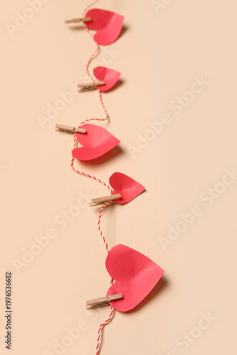 Red paper hearts hanging on rope against color background