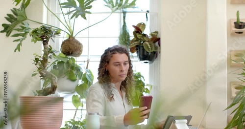 Nonbinary African American sitting at desk by window checking red phone tapping tablet using laptop