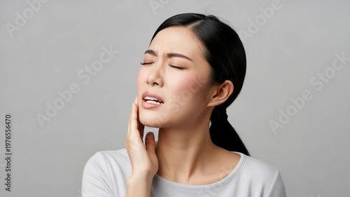Asian Woman Experiencing Tooth Pain Holding Cheek Against Gray Studio Backdrop For Dental Healthcare Advertisements Medical Illustrations