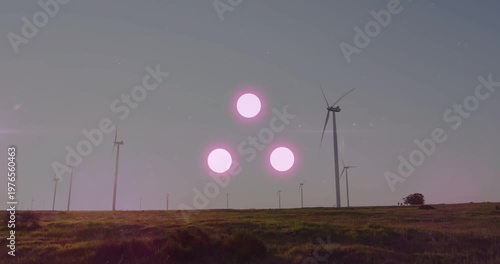 Late afternoon sunlight striking wind farm turbines creating pink flare triad peaking then fading