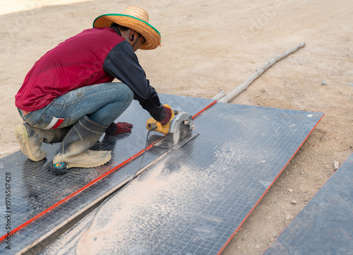 Construction worker using a circular saw to cut plywood on the ground.