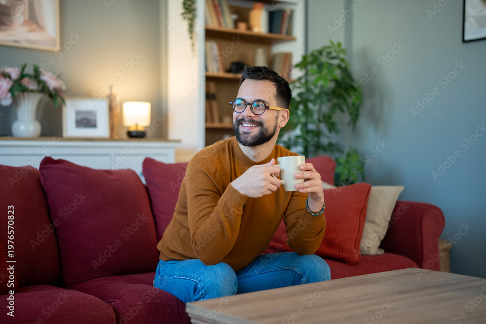 Obraz premium Man relaxing on sofa enjoying morning coffee at home