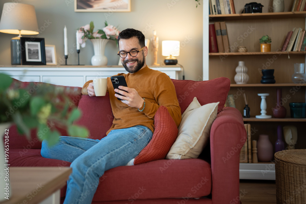 Obraz premium Man relaxing on sofa using smartphone enjoying leisure time
