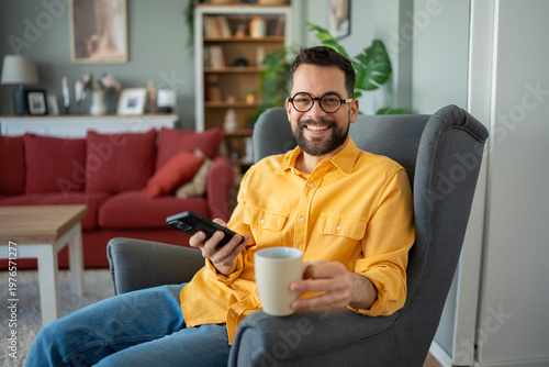 Quadro em tela Happy man relaxing at home holding phone and mug