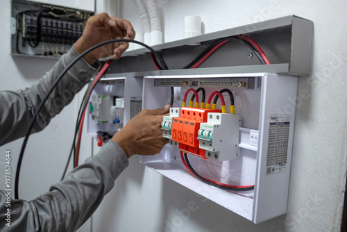 The electrician is connecting the electrical circuits in the control box of the solar power generation system and organizing the wiring in the control cabinet.