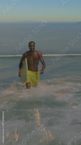 Vertical video: Surfer after ride, walking to shore, overlay flagging broken fins on yellow board