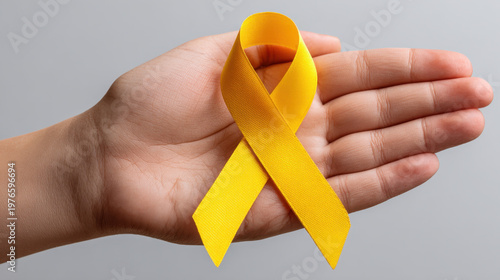 Hand holding yellow ribbon for awareness, close up on palm with support symbol on gray background