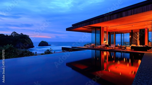 Luxurious modern dwelling overlooks ocean seascape at twilight with illuminated interior