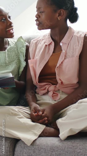 Vertical video: Turning teen in pink shirt responding to child showing open book at home, smiling