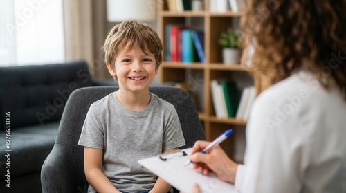 During a behavioral therapy session, a child smiles as the psychologist talks and observes, conducting a supportive assessment with a clipboard, couch, and bookshelf nearby.