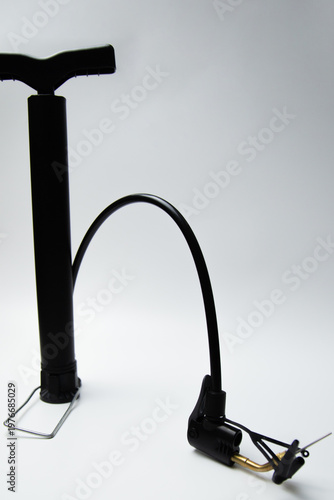 Vertical close-up photo of black pump hand pump with multiple attachments and leg handle lying on side on white background. High quality photo