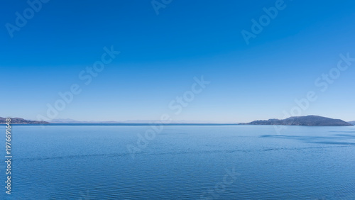 A beautiful alpine lake. The endless blue smooth surface of the water. Mountains on the horizon. Clear sky. Copy  space. Peru. Lake Titicaca.