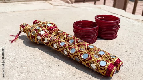 Ornate decorative textile with mirrored accents and stacked red glass bangles, traditional embellishment, cultural accessory, rich detail