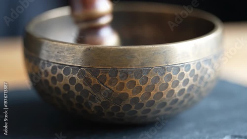 Tibetan singing bowl with wooden striker resting on dark slate, detailed hammered metal texture, peaceful meditation tool