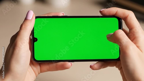 A person holding a smartphone horizontally with a green screen for chroma key compositing.