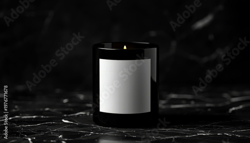 A lit candle in a black glass jar with a white label on a dark marble surface