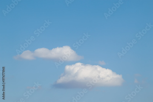 Two fluffy white cumulus clouds floating in a clear blue summer sky