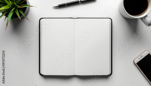 A well-organized workspace with a blank notebook, pen, plant, coffee, and smartphone on a clean white desk.
