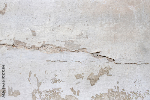 Cracked plaster wall showing peeling paint, surface damage and weathered text...